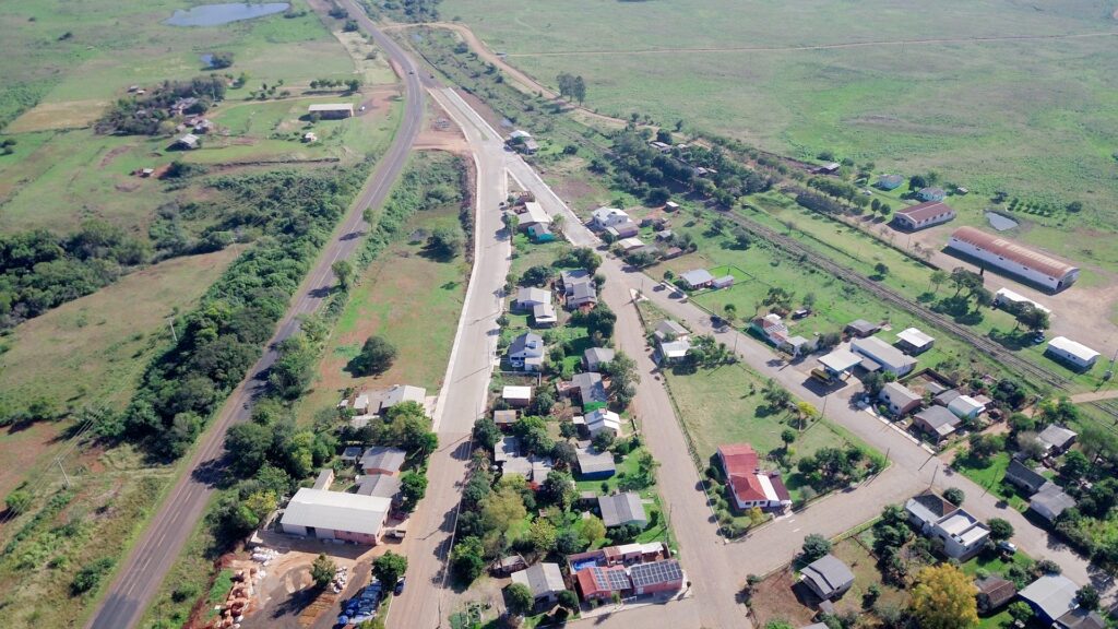 Vista aérea de cidade no centro do RS, com prédios baixos e campos verdes ao redor sob céu azul