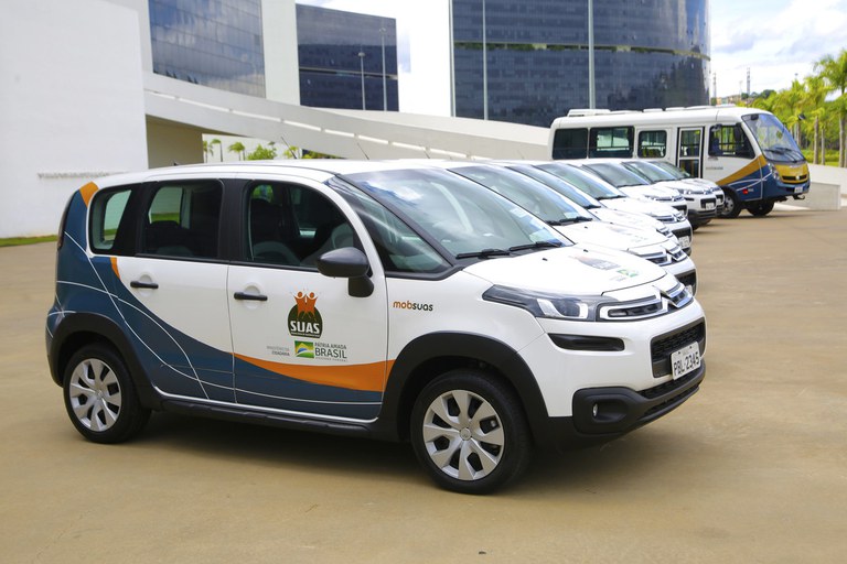 Veículos do SUAS estacionados em área urbana, ilustração de serviços socioassistenciais