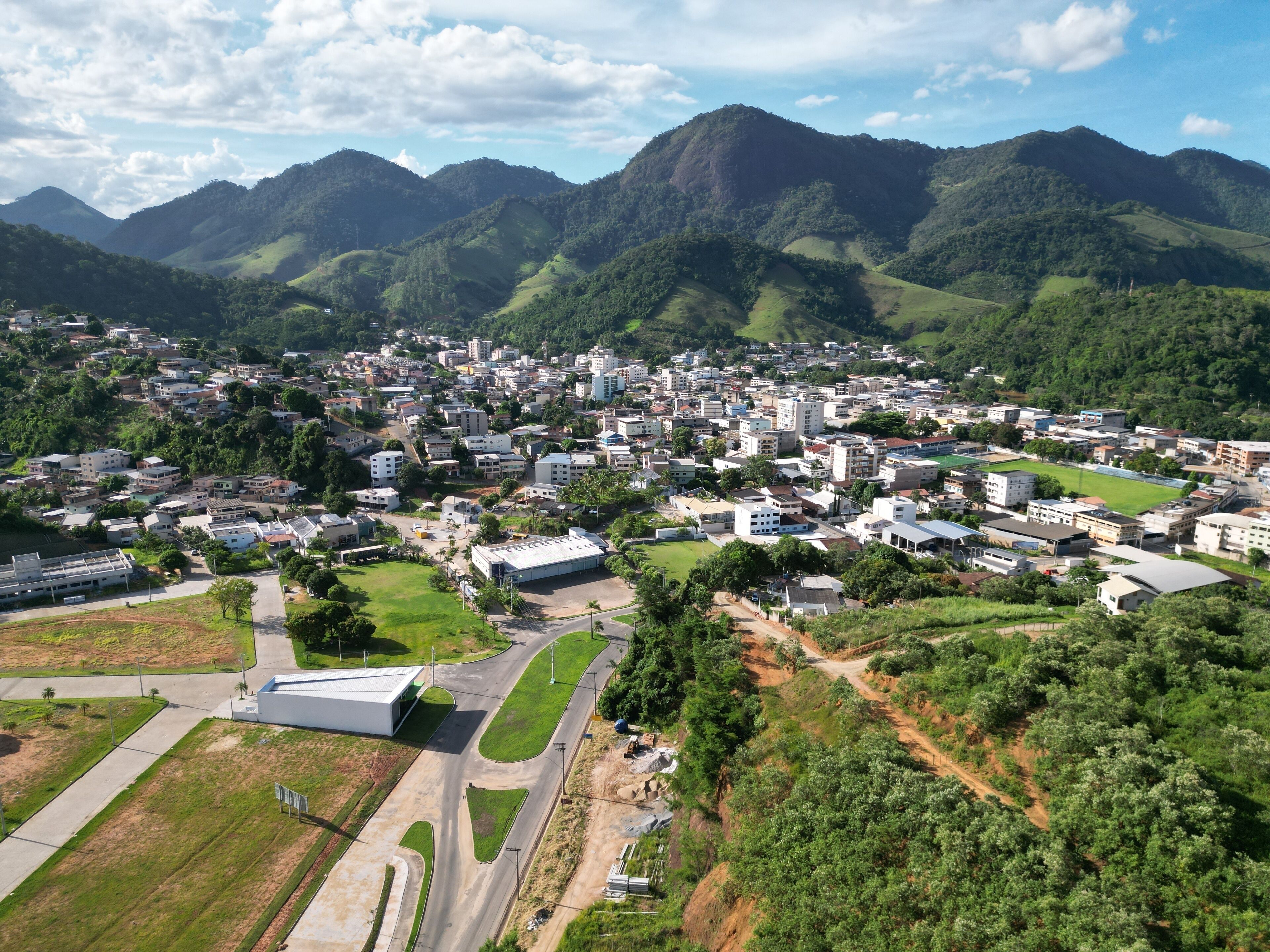 Vista aérea de cidade serrana com morros verdes, mostrando um vale urbano cercado por natureza em Alfredo Chaves ES.