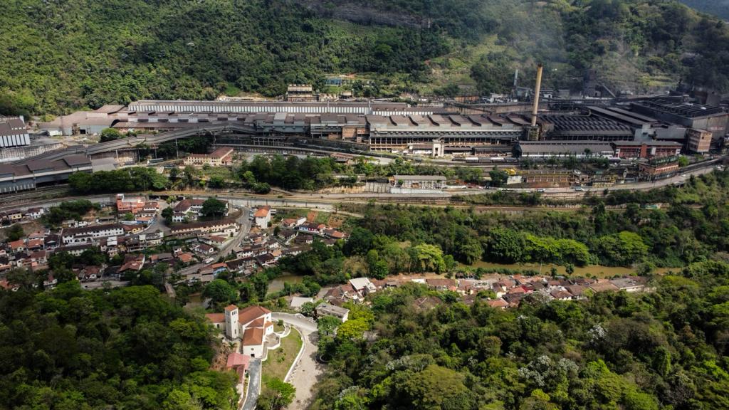 Vista urbana com indústrias e morros ao fundo, representando uma cidade média em Minas Gerais