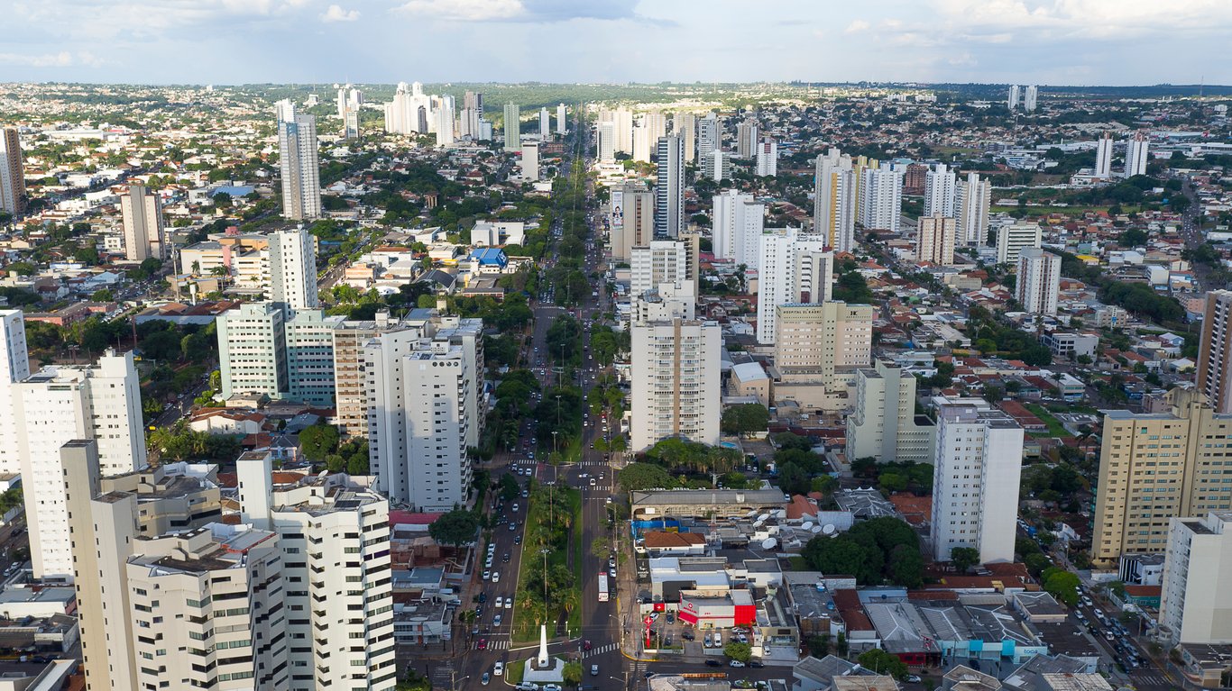 Vista aérea de Campo Grande MS ao pôr do sol, com áreas verdes e skyline baixo