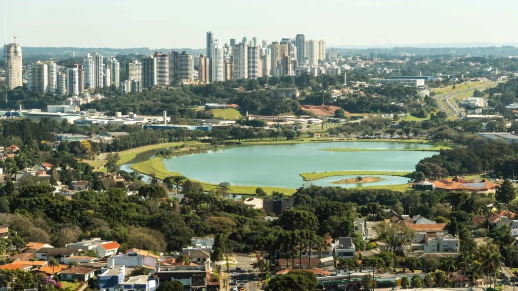 Vista aérea de cidade de pequeno porte com áreas verdes e lago, céu aberto e dia ensolarado