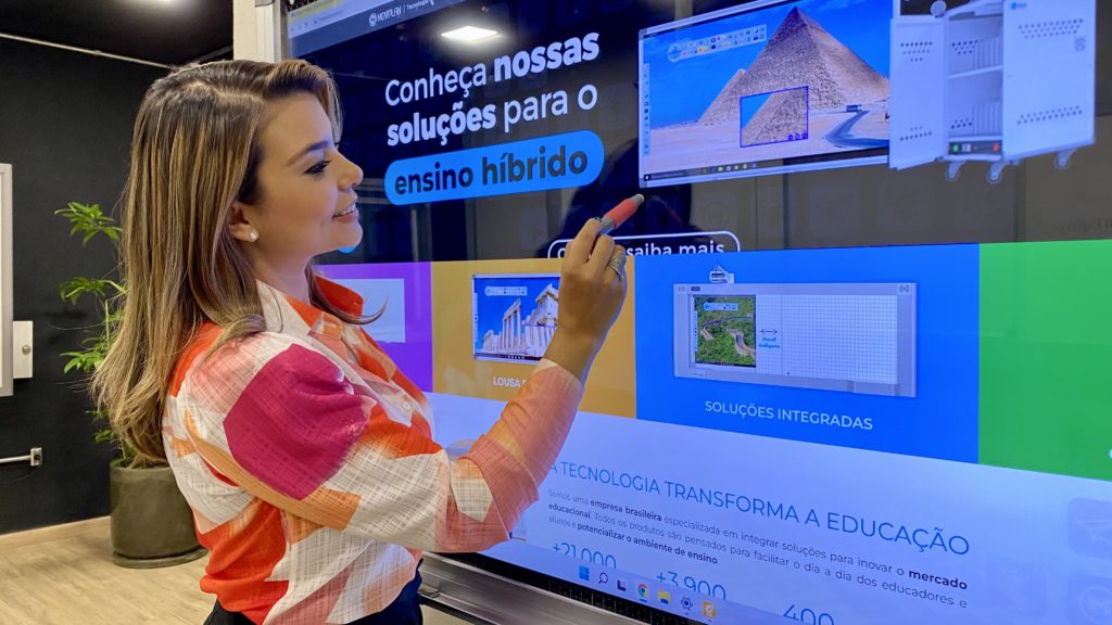 Sala de aula do ensino fundamental, professora na lousa e alunos em carteiras, ambiente claro e arejado