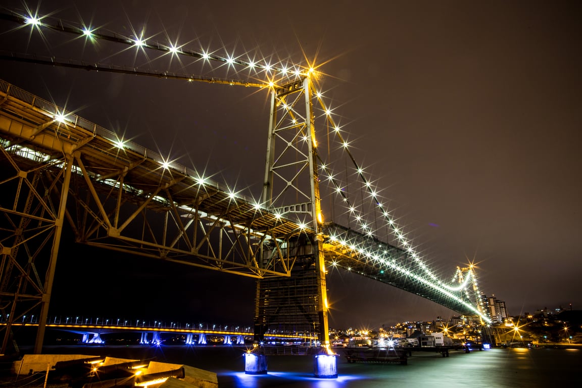 Vista de Florianópolis com a Ponte Hercílio Luz iluminada, em composição horizontal