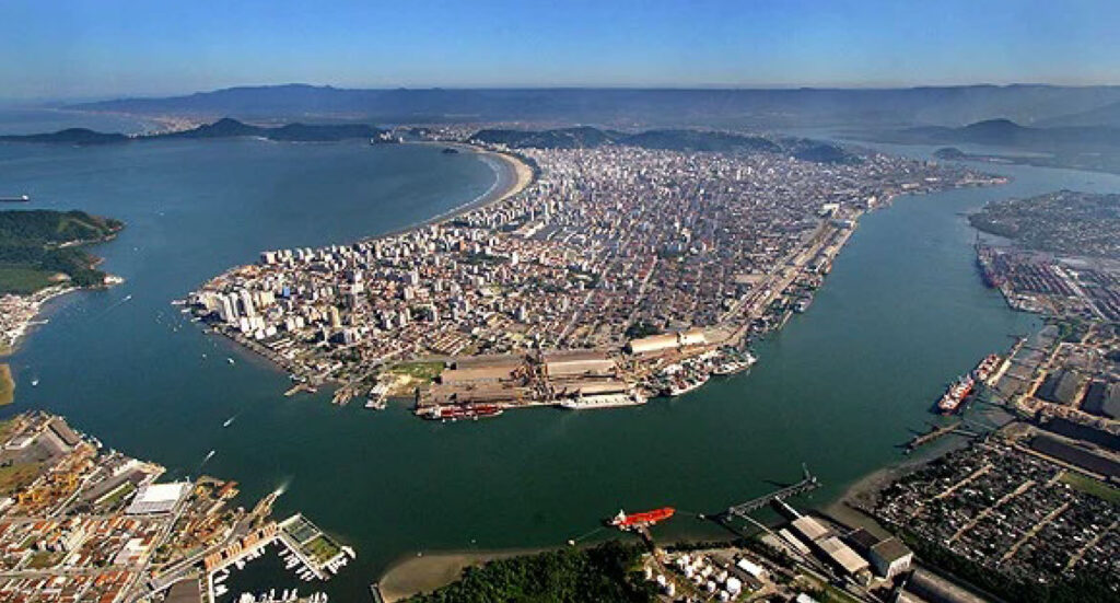 Vista aérea do Porto de Santos com a orla, navios e contêineres ao fundo, ao entardecer