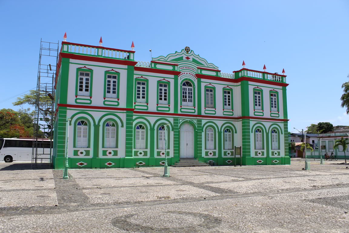 Fachada de prédio público municipal, com bandeiras e praça no entorno