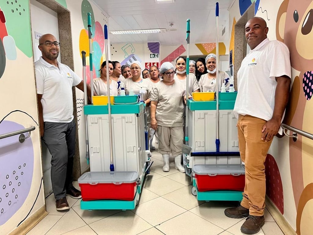 Corredor hospitalar com equipe de limpeza e carrinhos de higienização