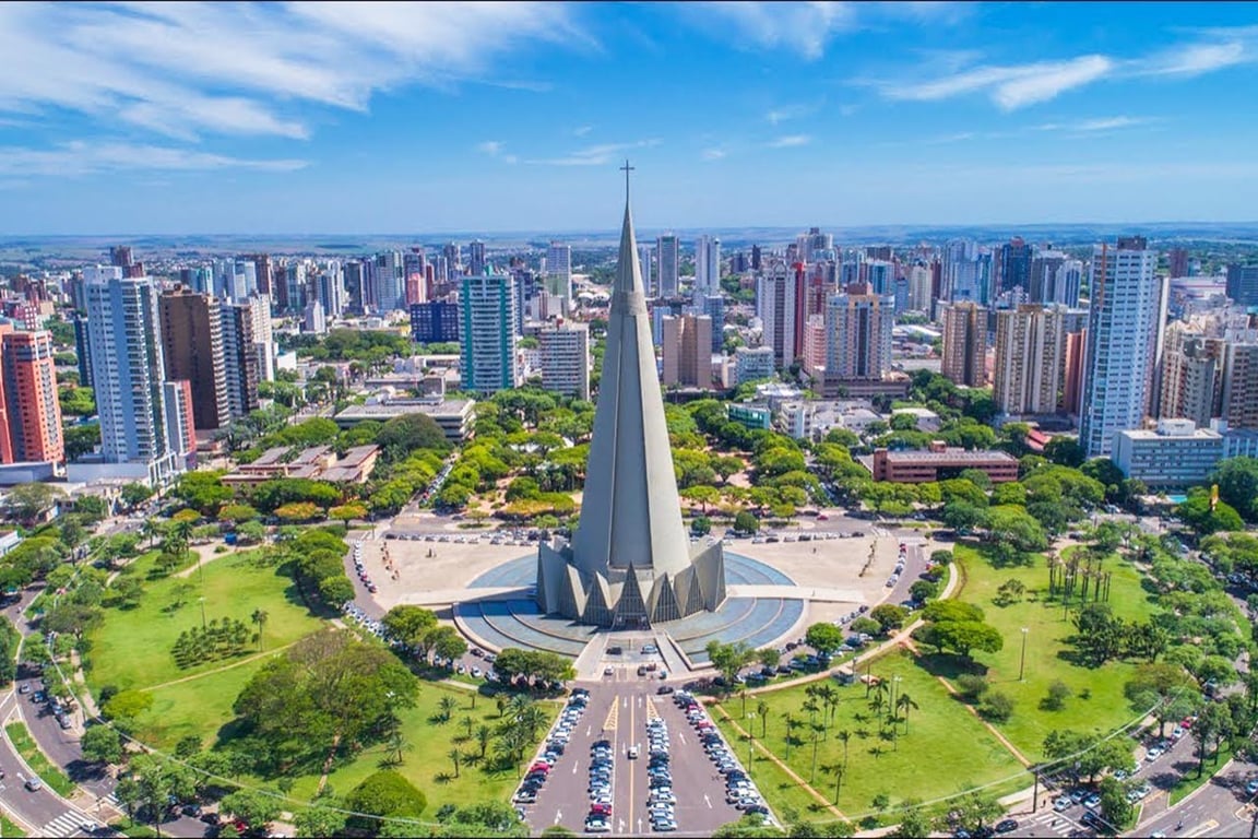 Centro urbano de município do interior do Paraná, com igreja e áreas verdes ao redor, sob céu azul com nuvens