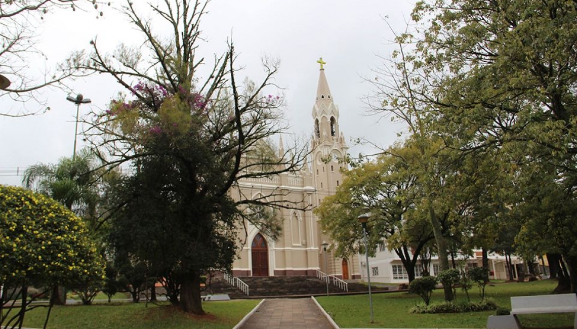 Praça arborizada e igreja ao fundo em cidade do interior do Rio Grande do Sul.