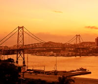 Vista aérea de Florianópolis ao pôr do sol, com ponte e costa ao fundo