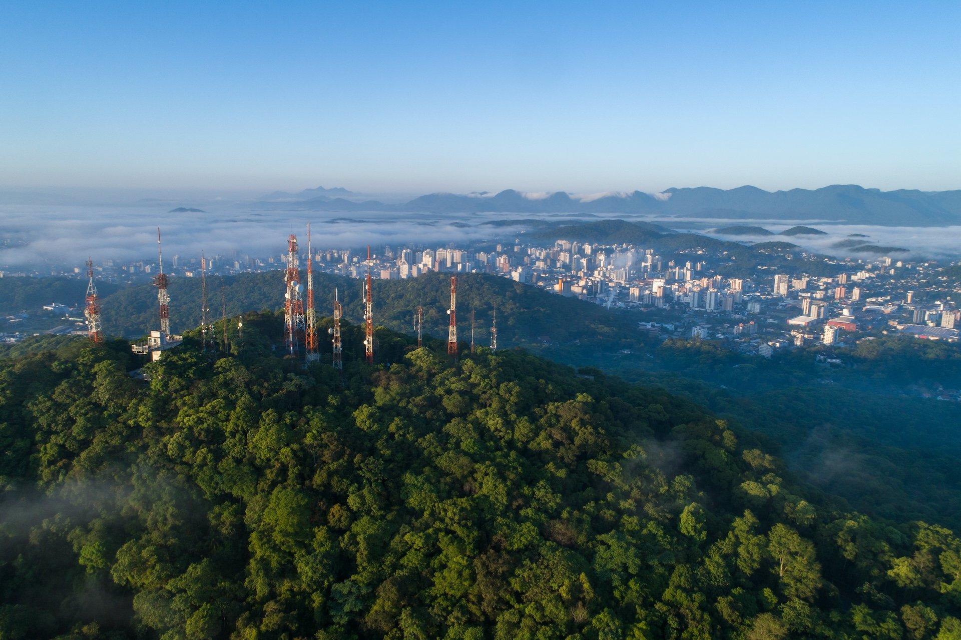 Vista aérea de Joinville SC ao entardecer, com skyline urbano e montanhas ao fundo
