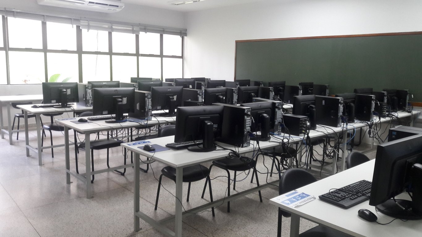 Ambiente acadêmico com laboratório de informática, mesas e computadores