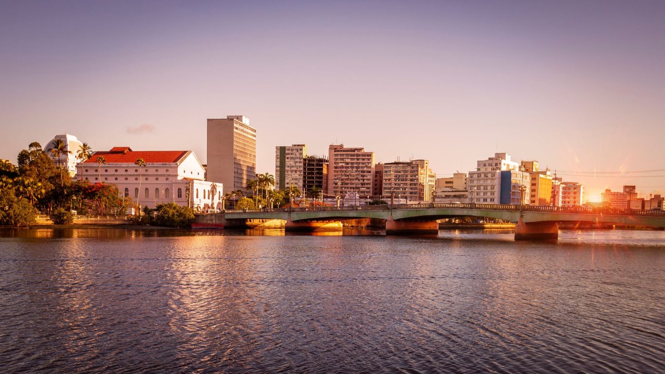 Recife vista aérea ao pôr do sol, com o Rio Capibaribe e prédios ao fundo