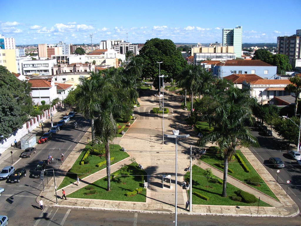 Praça central arborizada com prédios ao fundo em cidade do interior, fim de tarde