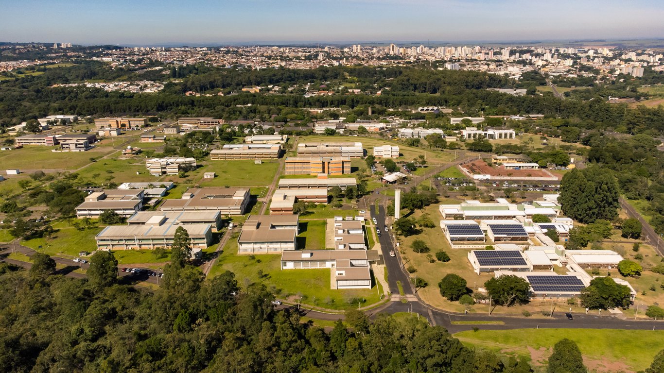 Vista aérea do campus da UFSCar em São Carlos, com prédios e áreas verdes ao fundo, em um dia claro