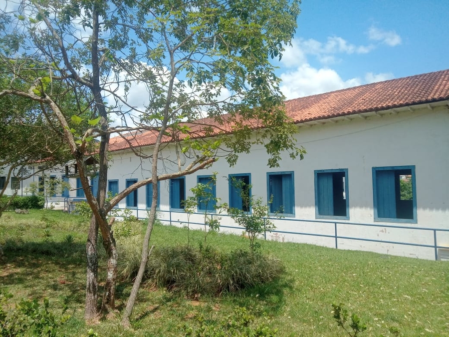 Prédio no campus da UFOP, com janelas azuis e área verde ao redor; estudantes circulam em dia ensolarado