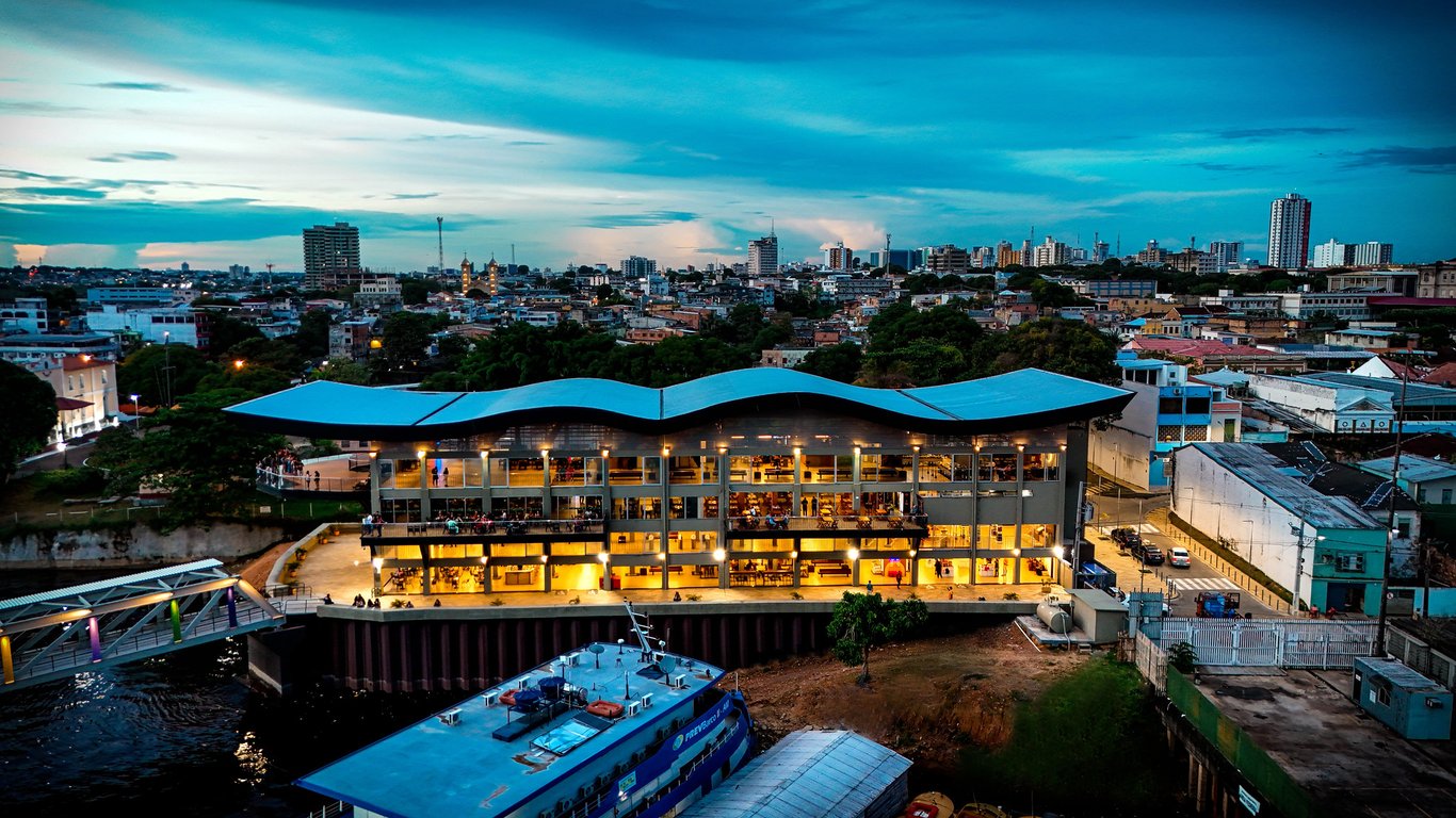 Vista aérea de Manaus ao pôr do sol, com a orla urbana e vegetação ao fundo