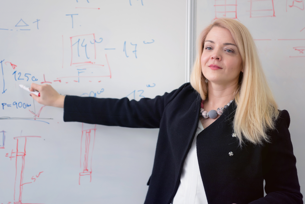 Sala de aula universitária com professor escrevendo equações no quadro