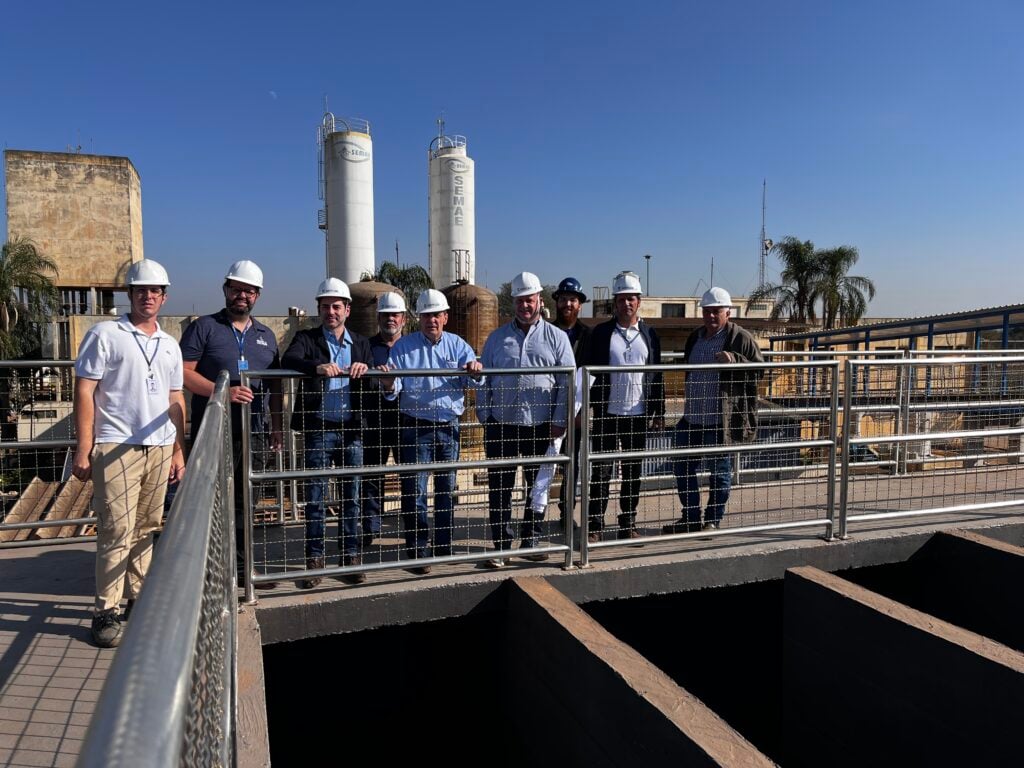 Equipe técnica em estação de tratamento de água, com passarelas e tanques metálicos