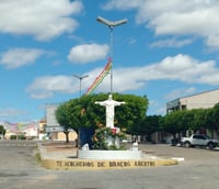 Praça central de Marcelino Vieira RN, com estátua ao centro, árvores e bandeirinhas decorativas sob céu aberto
