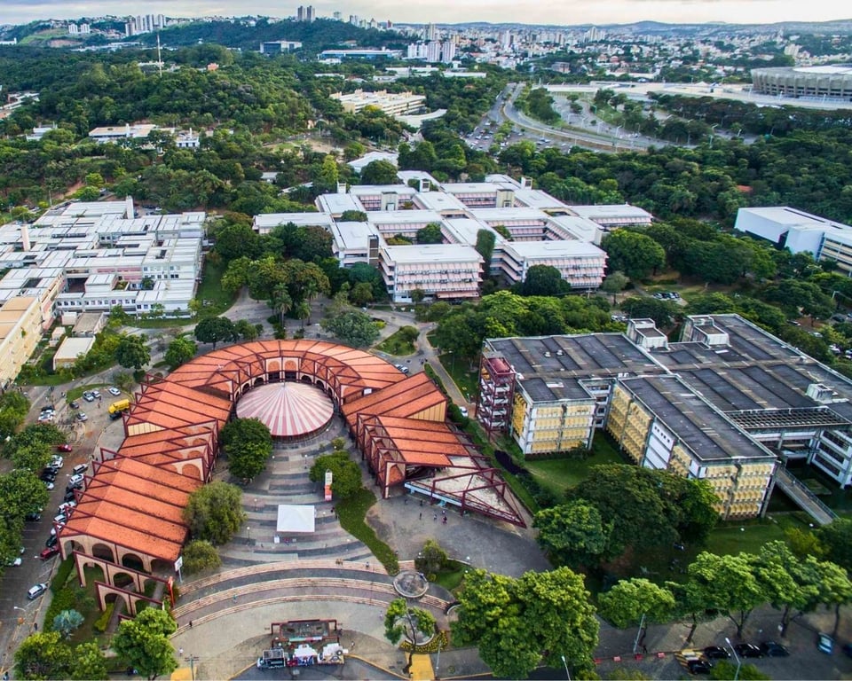Campus Pampulha da UFMG visto do alto, com áreas verdes, prédios acadêmicos e a Lagoa da Pampulha ao fundo