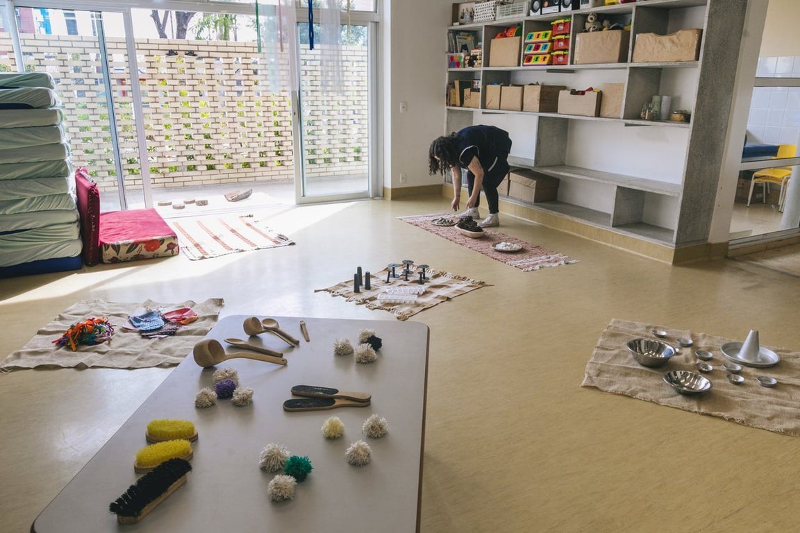 Sala colorida de Educação Infantil, com materiais lúdicos e educadora organizando o ambiente