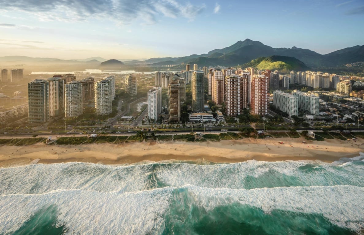 Vista urbana da Barra da Tijuca ao entardecer, com prédios e praia.