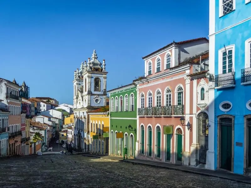 Vista urbana de pequena cidade do interior baiano, com casas coloridas e igreja ao fundo, sob céu azul.