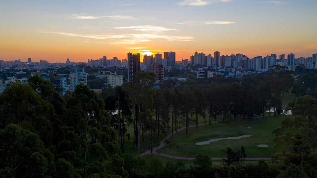 Vista panorâmica de Curitiba ao pôr do sol, com prédios e áreas verdes