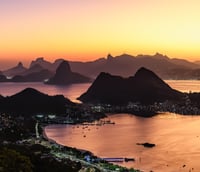 Vista panorâmica do Rio de Janeiro ao entardecer, com orla e montanhas ao fundo