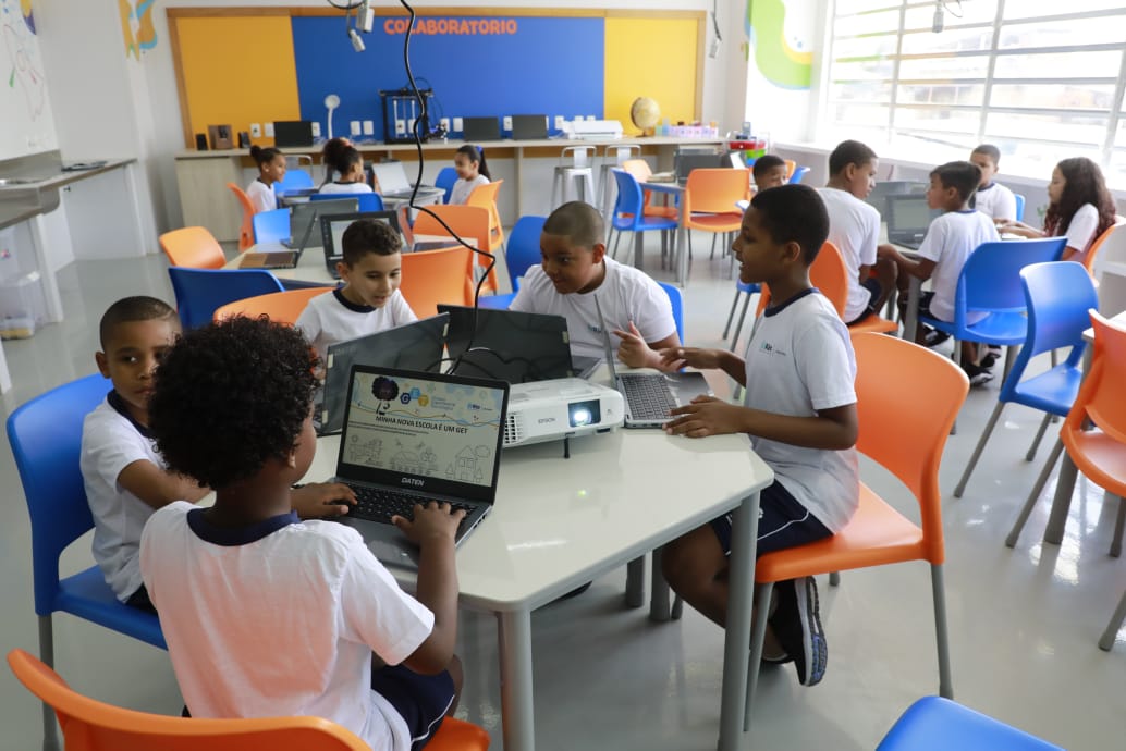 Sala de aula iluminada com carteiras organizadas e alunos usando laptops