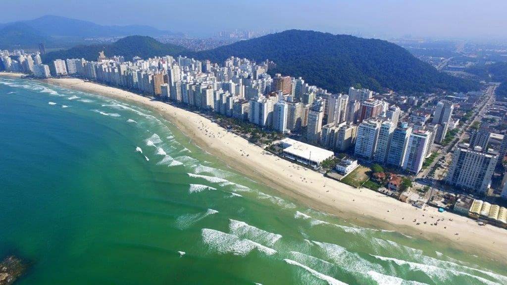 Vista aérea da orla de Guarujá com praias e prédios residenciais ao fim da tarde.