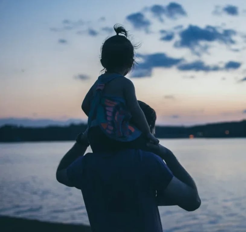 Father carrying his daughter on his shoulders at sunset
