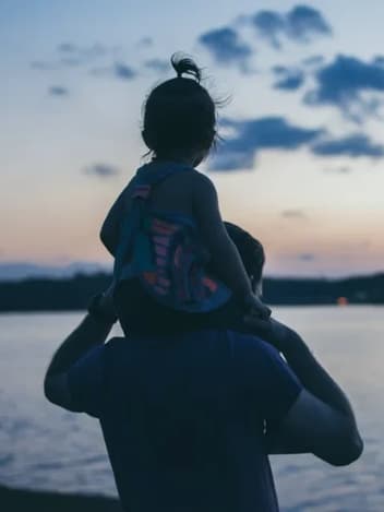 Padre llevando a su hija sobre los hombros al atardecer