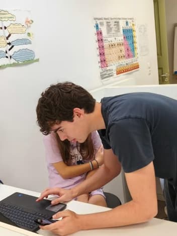 Student helping a classmate on a laptop