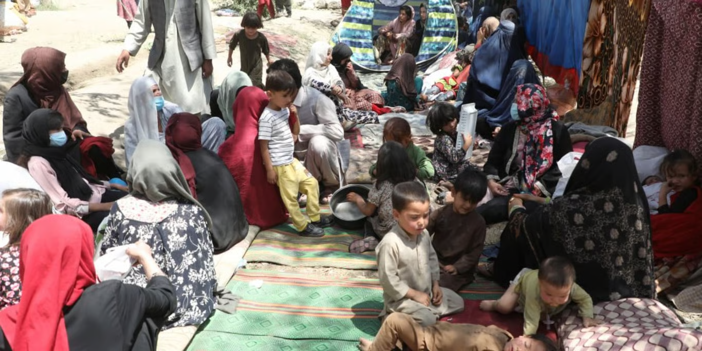 Displaced families with young children sheltering on mats at a makeshift camp