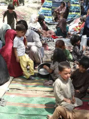 Displaced families with young children sheltering on mats at a makeshift camp