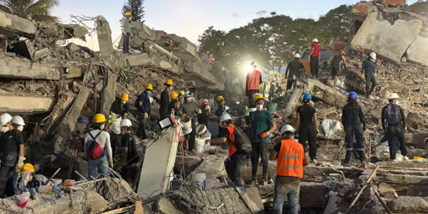 Rescue workers in hard hats searching the rubble of a collapsed building at dusk