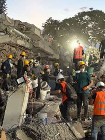 Rescue workers in hard hats searching the rubble of a collapsed building at dusk