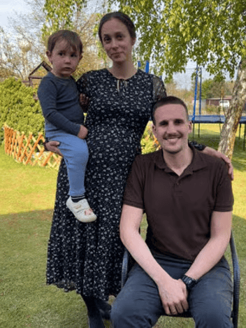 A family of three together in a garden, a parent holding a toddler beside a seated man
