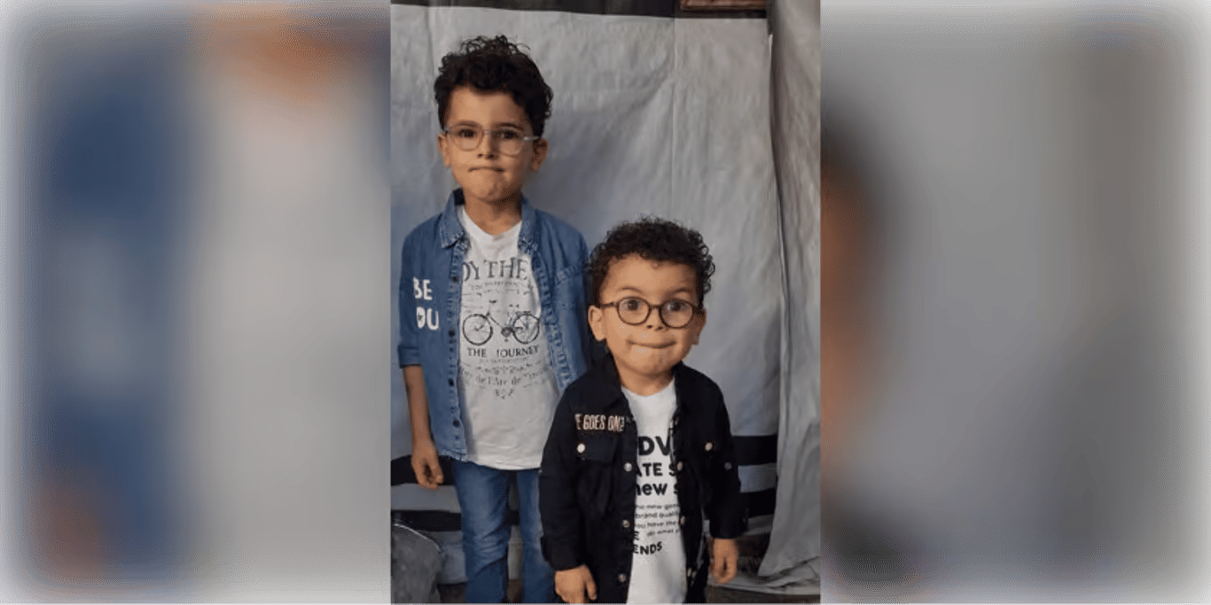 Two young boys in glasses standing in front of a tent wall