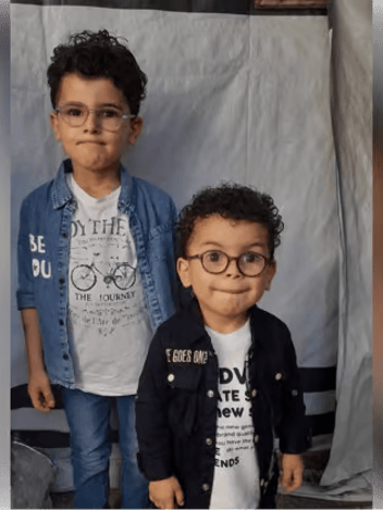 Two young boys in glasses standing in front of a tent wall