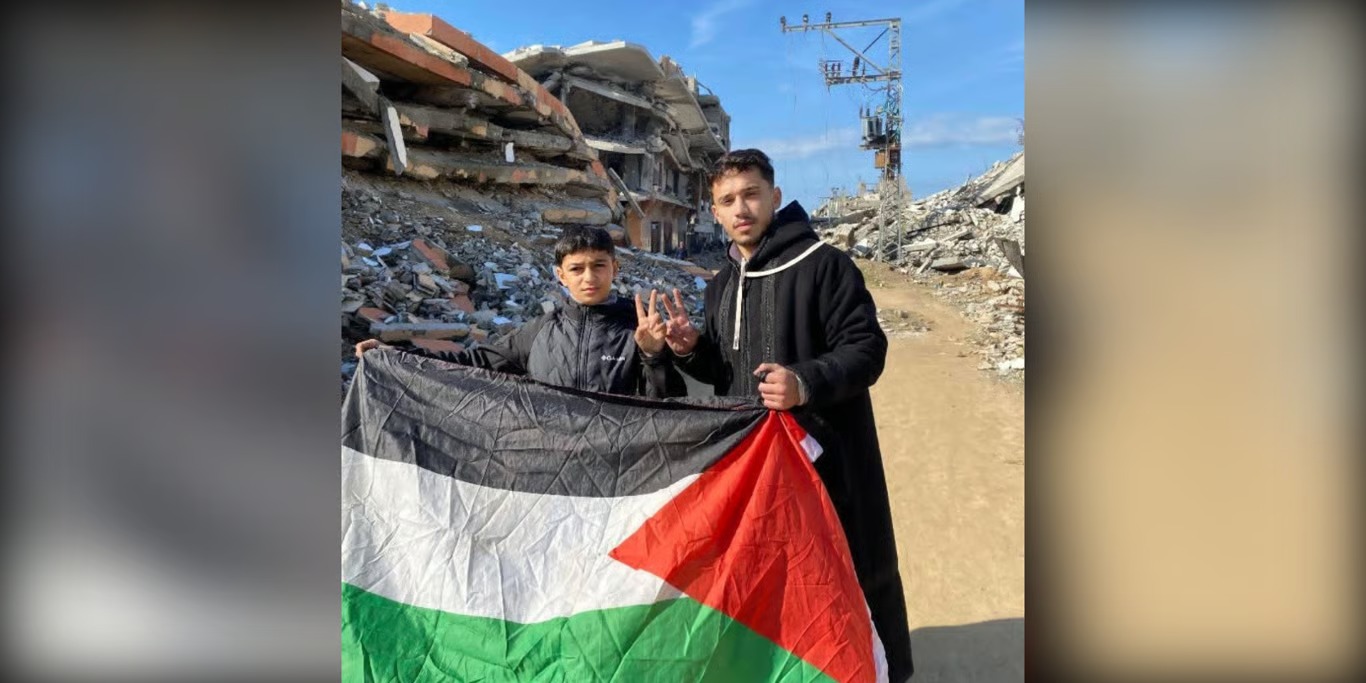 Two young men holding a flag in front of rubble