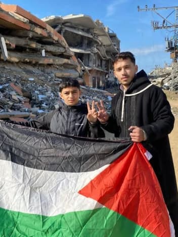 Two young men holding a flag in front of rubble