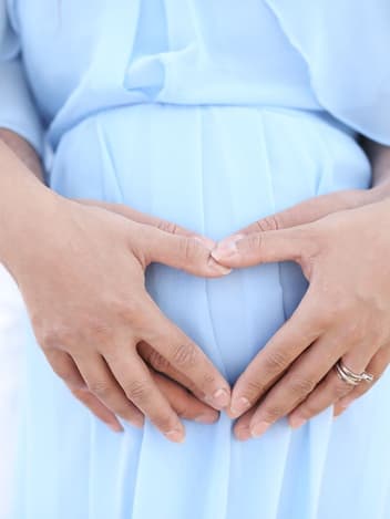Couple forming a heart with their hands over a pregnant belly
