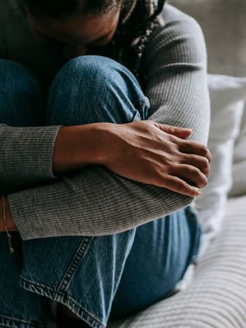 Woman hugging her knees on a sofa