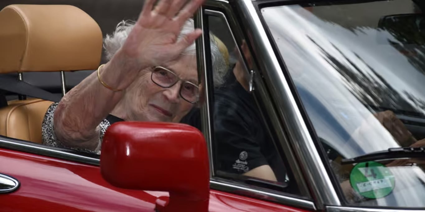 Elderly woman waving from a classic car