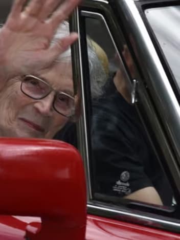 Elderly woman waving from a classic car