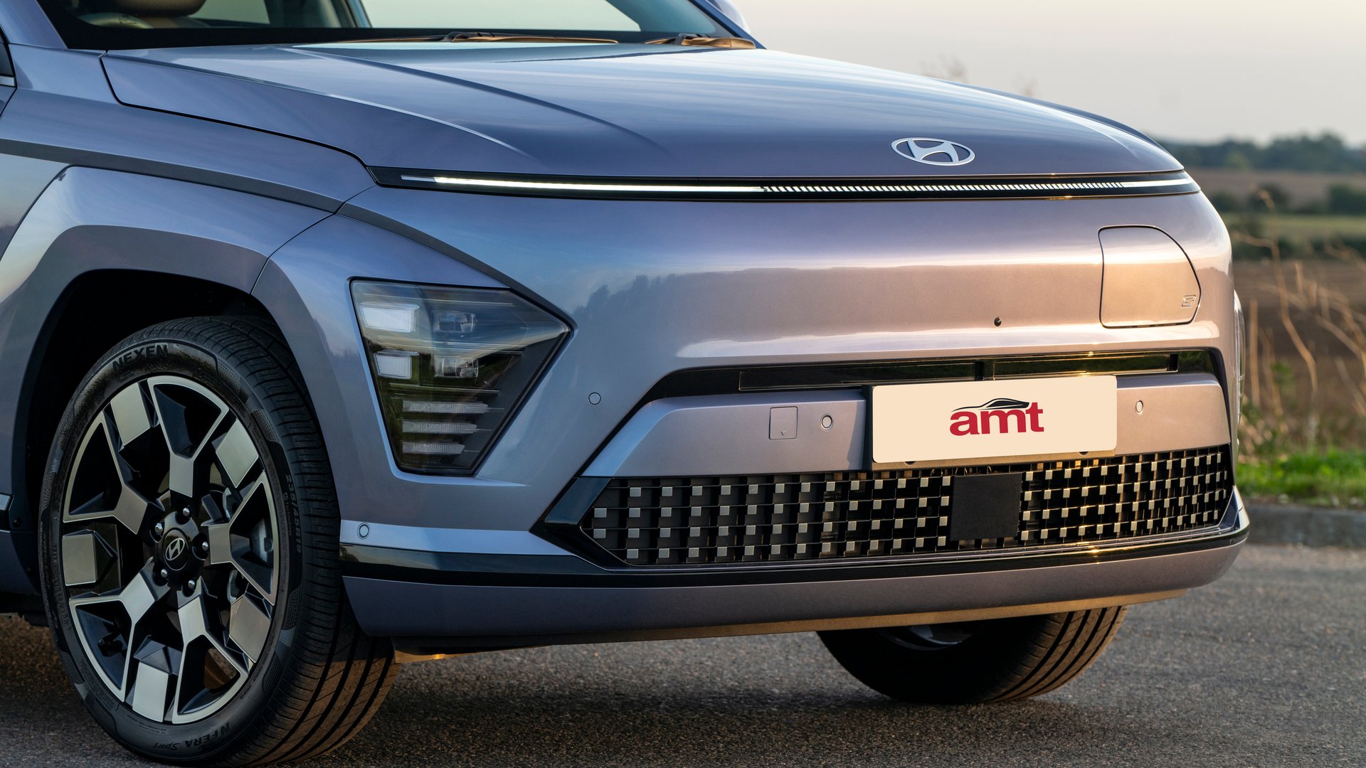 Close-up view of the Hyundai Kona Electric’s sleek front design, featuring a smooth grille-less bumper that enhances aerodynamics and energy efficiency, exemplifying modern style and practicality.