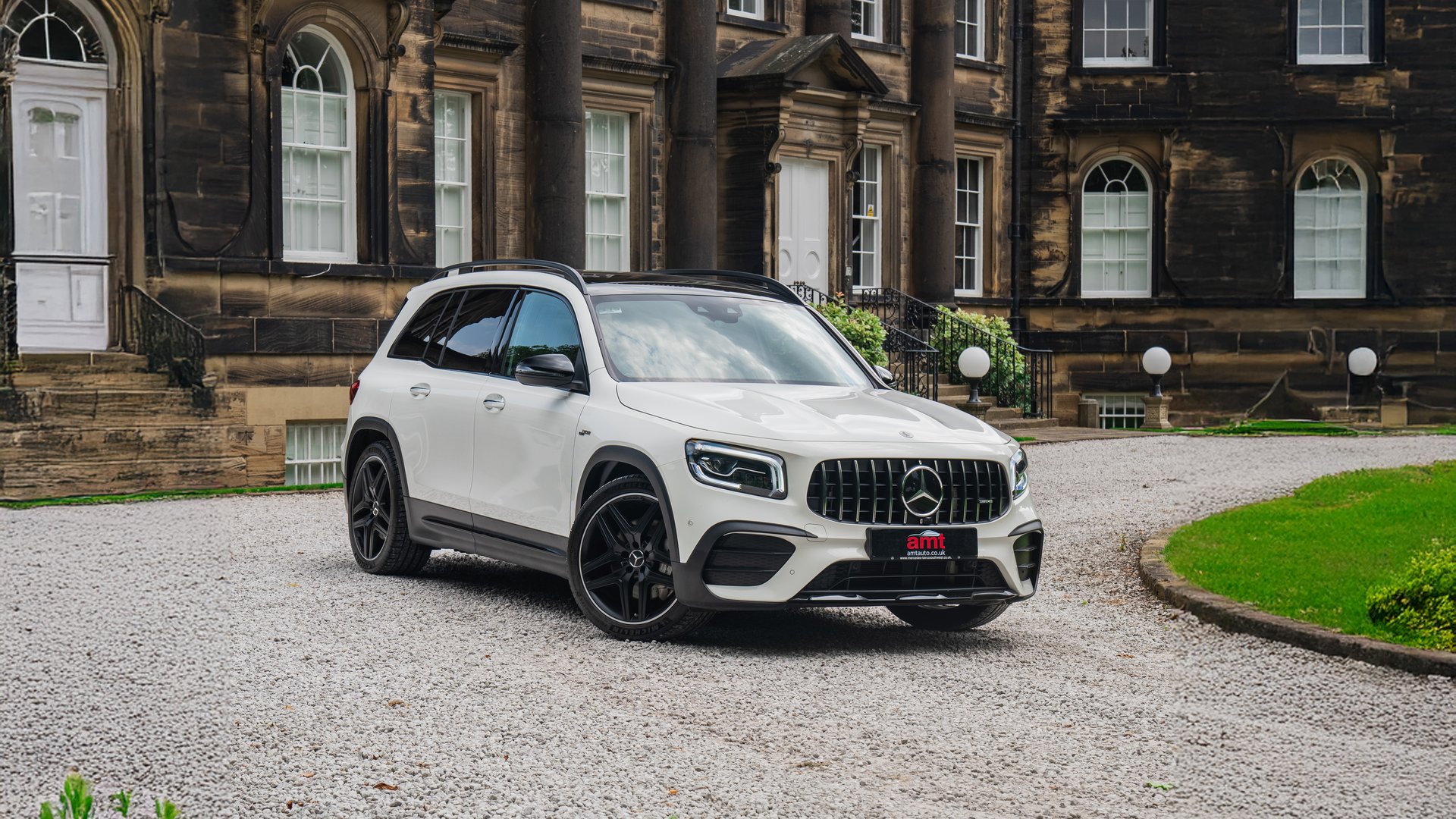 A white Mercedes GLB, a luxurious and compact 7 seater car, parked on a gravel driveway in front of an elegant historic building